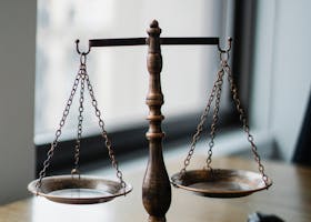 Decorative judgement scale and gavel placed on desk in light lawyer office against window